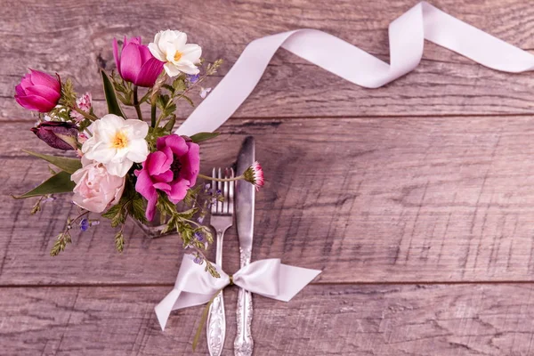 Coloque los ajustes de la mesa con tenedor y cuchillo, atado con una cinta de satén blanco, y las flores en una vista superior de la mesa vintage, la puesta plana, vista aérea — Foto de Stock