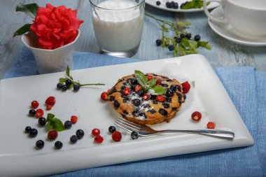 Berry muffin böğürtlen ve çilek beyaz bir tabak ve süt ile hizmet ve pembe ahşap bir masa ile bir vazoda gül