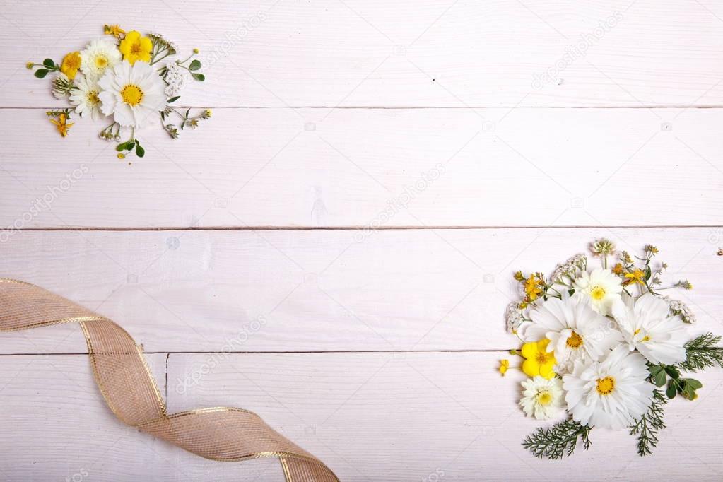 A bouquet of white flowers cosmea or cosmos with ribbon on white boards. Garden yellow flowers over handmade wooden table background. Backdrop with copy space.