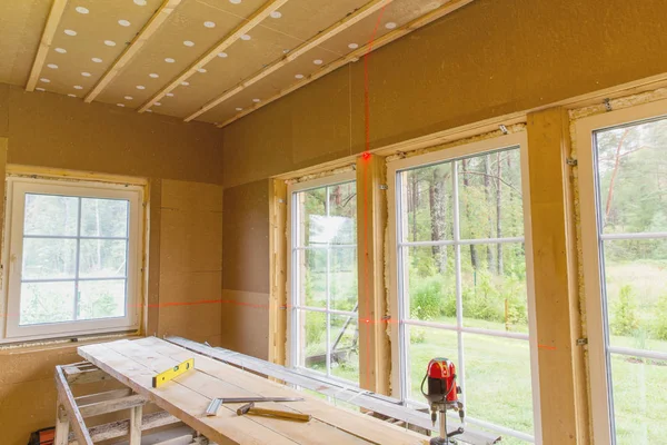 Bouwwerkzaamheden, afwerking van werk in een houten huis en installeren van windows met behulp van het niveau van de laser-lijn — Stockfoto