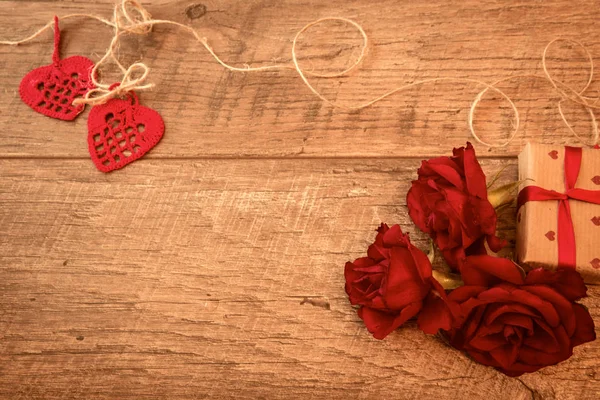 Composición en una mesa de madera con rosas rojas, regalo, corazones de ganchillo, y cintas. Concepto de San Valentín, fondo festivo — Foto de Stock