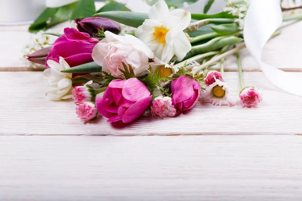 Ramillete de flores primaverales, tulipanes rosa, púrpura, narcisos y margaritas sobre fondo de madera blanca . — Foto de Stock