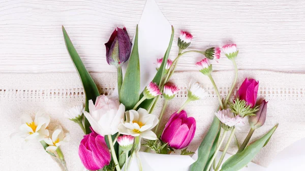 Ramillete de flores primaverales, tulipanes rosa, púrpura, narcisos y margaritas sobre fondo de madera blanca . — Foto de Stock