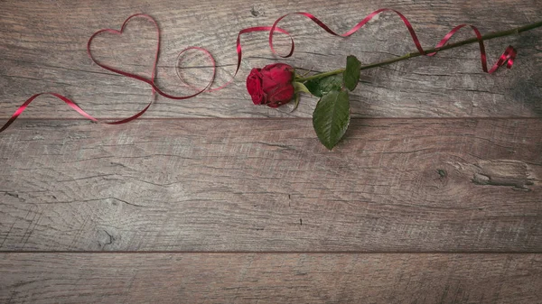 La cinta roja está forrada en el corazón de la forma en una mesa de madera oscura. Fondo de San Valentín, estilo rústico. Día de San Valentín lugar de mesa con rosa roja y cinta. Piso tendido, vista superior . — Foto de Stock