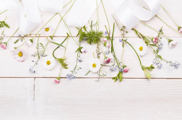 Delicadas flores blancas, azules, rosadas y cinta blanca sobre tabla de madera blanca. Vista superior, posición plana. Copiar espacio. Cumpleaños, Dia de la madre, San Valentín, Mujeres, concepto de día de la boda . — Foto de Stock