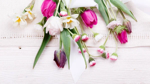 Kytice první jarní květy, růžové, fialové tulipány, narcisy a sedmikrásky na bílém pozadí dřevěná. — Stock fotografie