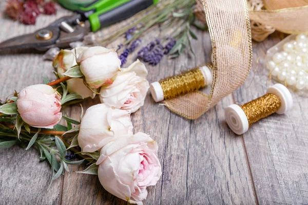 Flores, herramientas, cintas, rosas, lavanda, hierbas, verduras en la mesa de floristas en floristería. Mesa de estilo rústico de madera, espacio de trabajo . — Foto de Stock