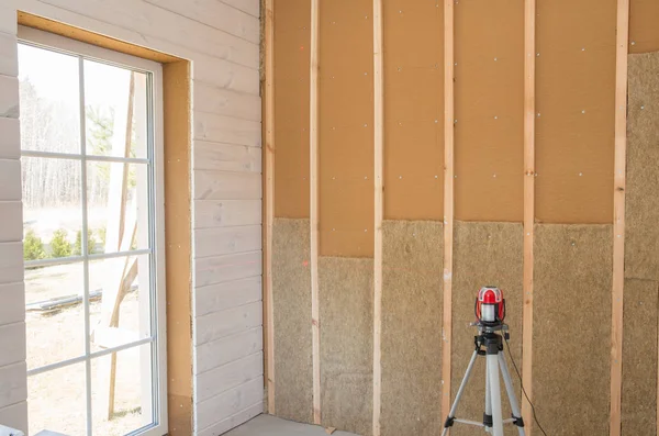 Bauarbeiter wärmeisolierendes Öko-Holzrahmenhaus mit Holzfaserplatten und wärmeisolierendem natürlichen Hanfmaterial. Endbearbeitung der Wände mit einer weißen Holzplatte mittels Laserlinienwaage — Stockfoto