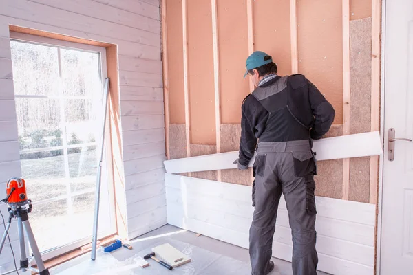 Stellt der Arbeiter die Nachbearbeitungsarbeiten der Wände mit dem weißen Holzbrett her, die Ebene der Laserlinie verwendend. Gebäude wärmeisolierendes Öko-Holzrahmenhaus mit Holzfaserplatten — Stockfoto