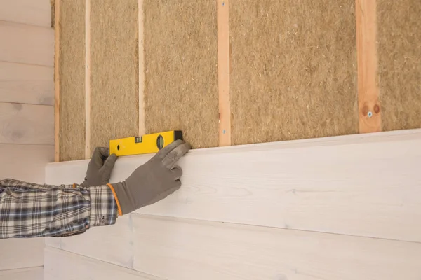 Stellt der Arbeiter die Nachbearbeitungsarbeiten der Wände mit dem weißen Holzbrett her, die Ebene der Laserlinie verwendend. Gebäude wärmeisolierendes Öko-Holzrahmenhaus mit Holzfaserplatten — Stockfoto