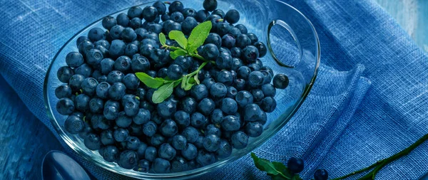 Freshly blueberries in glass bowl. Juicy and fresh blueberries with green leaves on blue wooden table. Concept for healthy eating and nutrition. — Stock Photo, Image