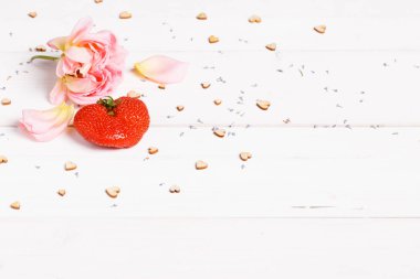 Pembe gülden yapılmış çerçeve, taç yaprakları, tahta beyaz arka planda kalp şeklinde kırmızı çilekler..