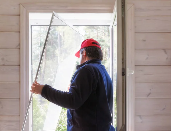 Worker install mosquito net or mosquito wire screen on wooden house window.