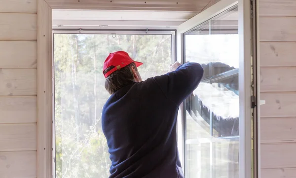 Robotnik instaluje moskitierę lub moskitierę na oknie drewnianego domu. — Zdjęcie stockowe