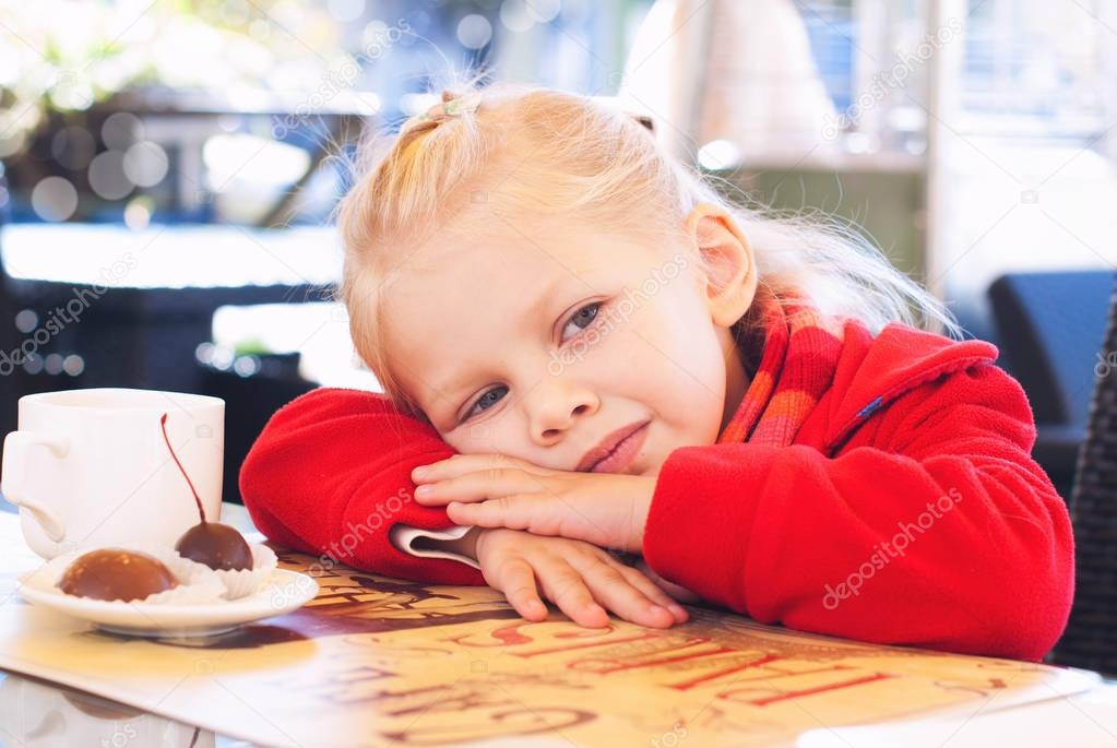 Little Girl Eats Sweets and Drinks Tea in Cafe.