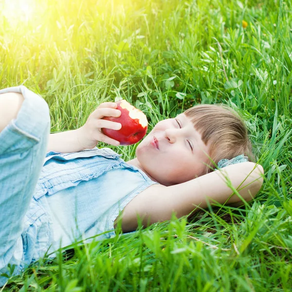 漂亮的女孩在草地上吃红苹果。快乐的孩子概念. — 图库照片