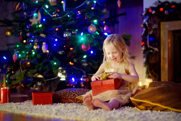 Girl opening Christmas gift by a fireplace — ストック写真