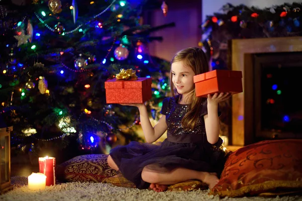 Chica abriendo regalos de Navidad junto a una chimenea — Foto de Stock