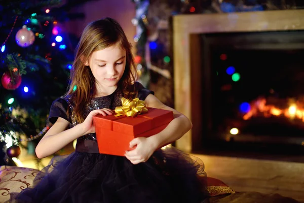 Girl opening Christmas gift by a fireplace — ストック写真