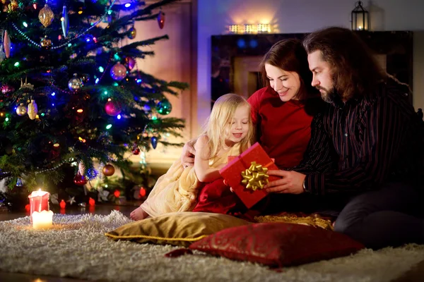 Family unwrapping Christmas gifts by a fireplace — Stock fotografie