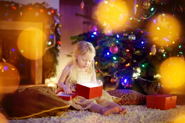 Girl opening Christmas gift by a fireplace — Φωτογραφία Αρχείου