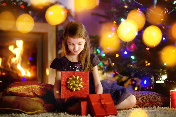 Girl opening Christmas gift by a fireplace — Stock fotografie