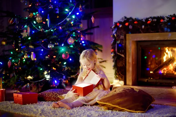 Girl opening Christmas gift by a fireplace — Stock Photo, Image