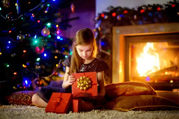 Girl opening Christmas gift by a fireplace — Φωτογραφία Αρχείου