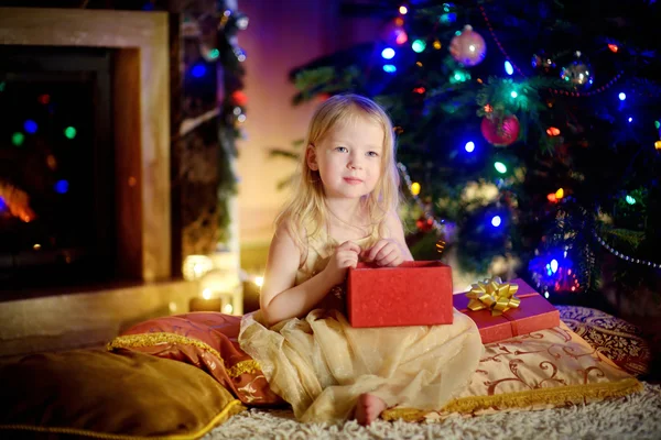 Girl opening Christmas gift by a fireplace Stock Photo