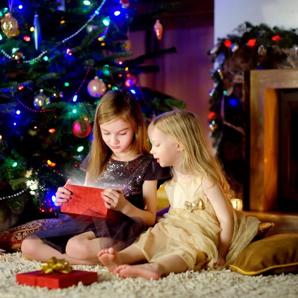 Hermanas abriendo regalo mágico de Navidad junto a una chimenea — Foto de Stock