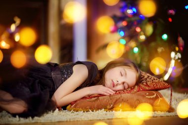 Noel ağacının altında bir şöminenin yanında uyuyan sevimli küçük kız