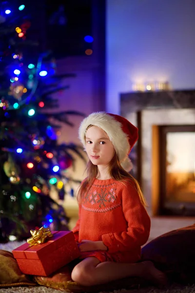 Menina feliz abrindo presentes de Natal por uma lareira — Fotografia de Stock