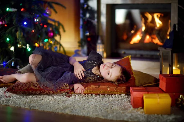 Happy girl opening Christmas gifts by a fireplace — Stock Photo, Image