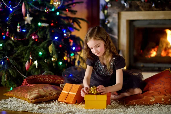 Menina feliz abrindo presentes de Natal por uma lareira — Fotografia de Stock