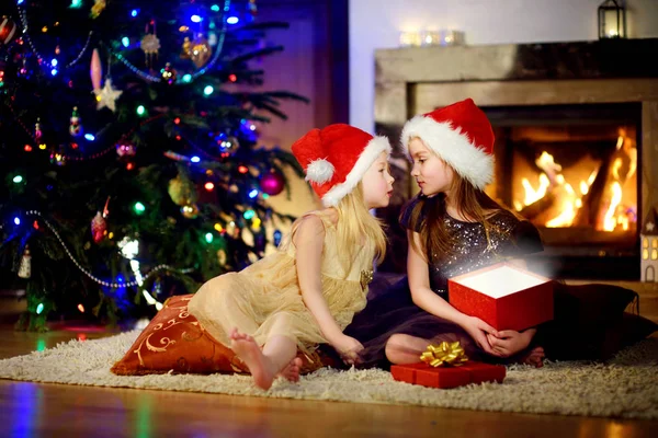 Sisters opening magical Christmas gift by a fireplace — Stock Photo, Image