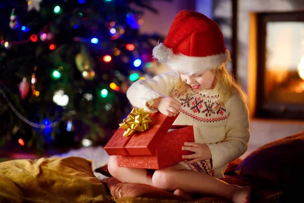 Menina feliz abrindo presentes de Natal por uma lareira — Fotografia de Stock