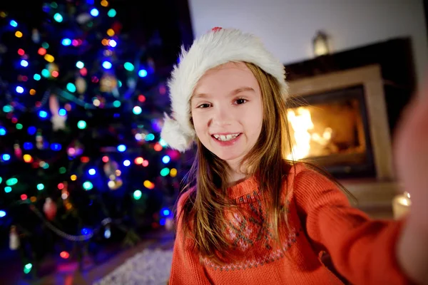 Boldog kis lány vesz egy selfie, egy díszített karácsonyi fa — Stock Fotó