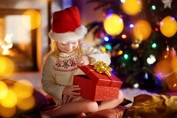 Menina feliz abrindo presentes de Natal por uma lareira — Fotografia de Stock