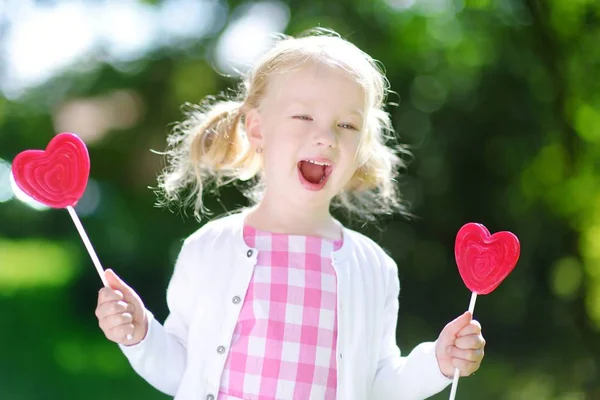 Liten flicka äter hjärtformade lollipop — Stockfoto