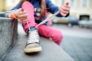 girl learning to tie shoelaces outdoors clipart