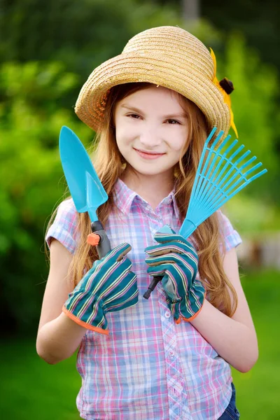 Niña usando sombrero de paja sosteniendo herramientas de jardín — Foto de Stock