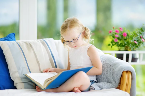 Маленькая девочка в очках читает книгу — стоковое фото
