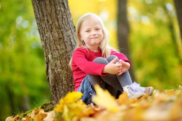 Mädchen sitzt auf Laub im Park — Stockfoto