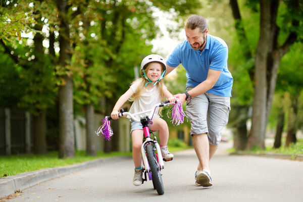 Отец учит дочь кататься на велосипеде