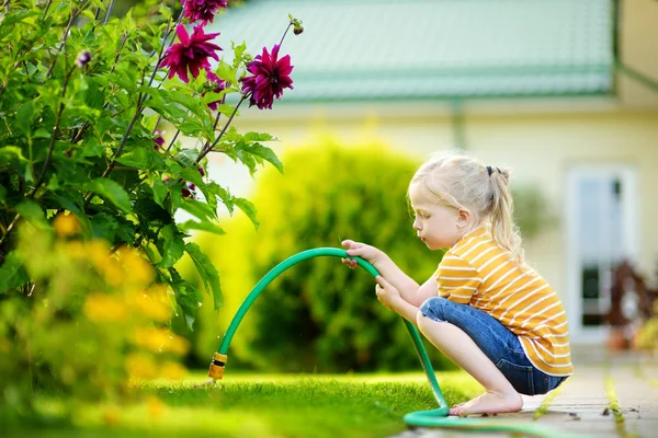 Malá dívka zalévání fialové květiny — Stock fotografie