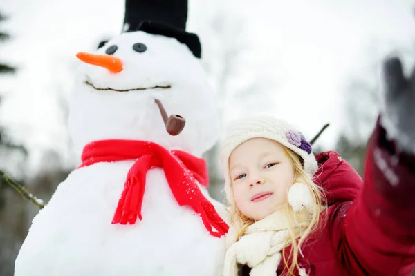 Adorable niña construyendo un muñeco de nieve —  Fotos de Stock