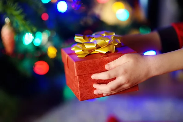Criança segurando um presente por uma árvore de Natal — Fotografia de Stock
