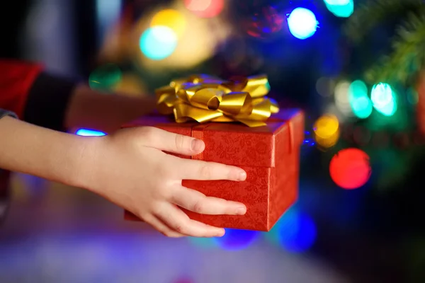 Criança segurando presente pela árvore de Natal — Fotografia de Stock