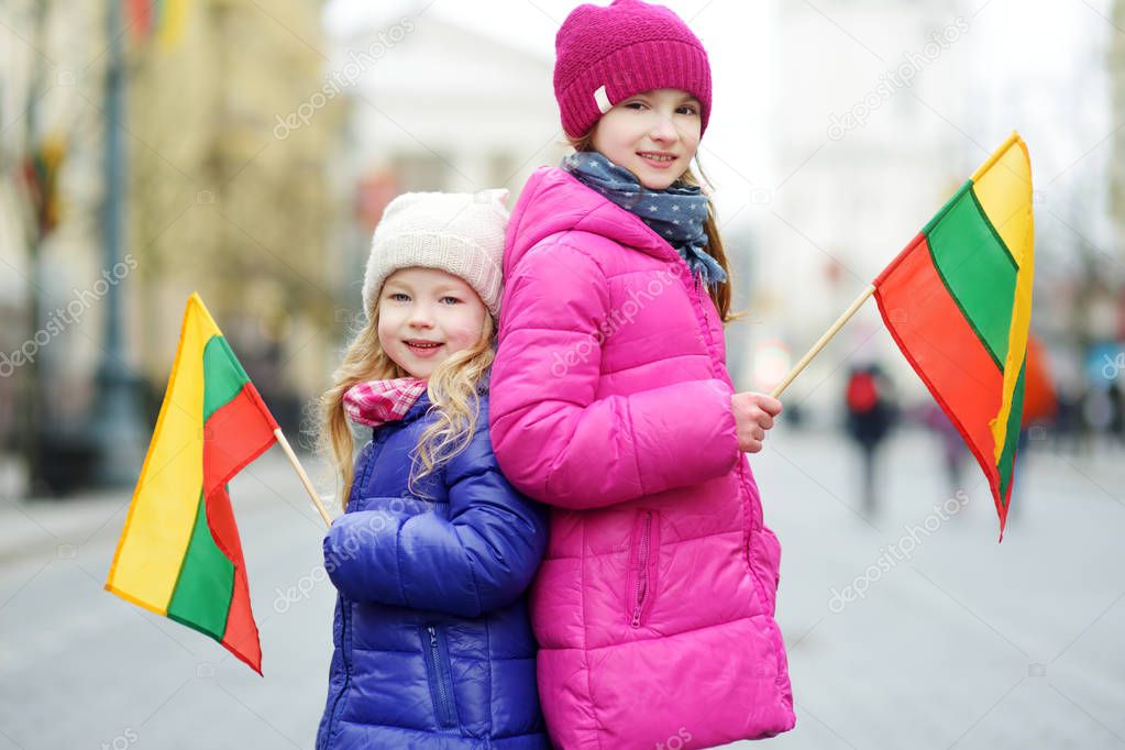 Two adorable little sisters celebrating Lithuanian Independence Day holding tricolor Lithuanian flags in Vilnius