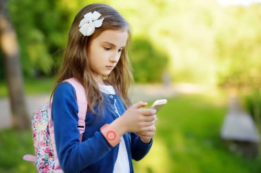 Sevimli küçük kız güzel yaz gününde bir akıllı telefon ile fotoğraf çekme. Mobil cihazlar kullanarak çocuklar.